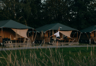 Personne jouant au frisbee devant des tentes glamping dans un parc de vacances entouré de verdure.