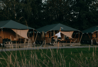 Persona che gioca con un frisbee davanti a tende glamping in un parco vacanze immerso nel verde.