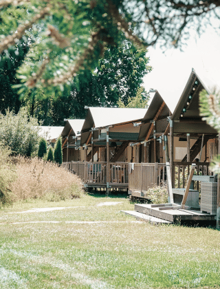 Glamping-accommodaties in een vakantiepark omgeven door groen en bomen op een zonnige dag.