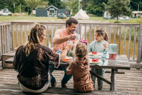 Una familia desayuna junta en una mesa de madera al aire libre en un parque vacacional de glamping.