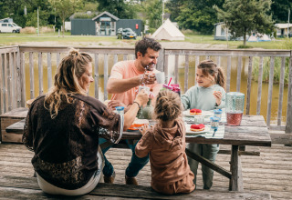 Une famille prend le petit-déjeuner dehors sur une table en bois, dans un parc de vacances glamping.
