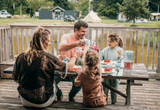 Une famille prend le petit-déjeuner dehors sur une table en bois, dans un parc de vacances glamping.