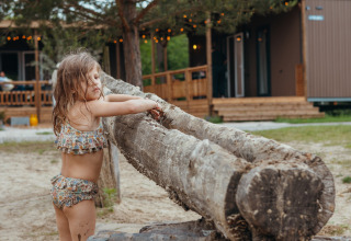Petite fille en maillot de bain près d’une grosse souche devant des lodges glamping dans un parc.