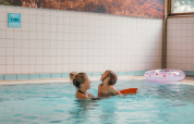 Mère et enfant profitent d’une piscine intérieure dans un parc de glamping, avec une bouée à proximité.
