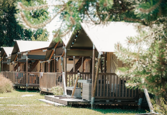Rangée de tentes safari avec terrasses en bois au Safari Cottage, entourées d’herbe et d’arbres verts.