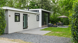 Moderne River Cabin met bubbeltub-Lodge mit Terrasse, Gartenmöbeln und Bäumen in grüner Umgebung.
