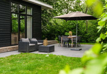 Buitenterras bij River Cabin met lounge stoelen, eettafel en parasol in Holiday Park Mölke, Nederland.