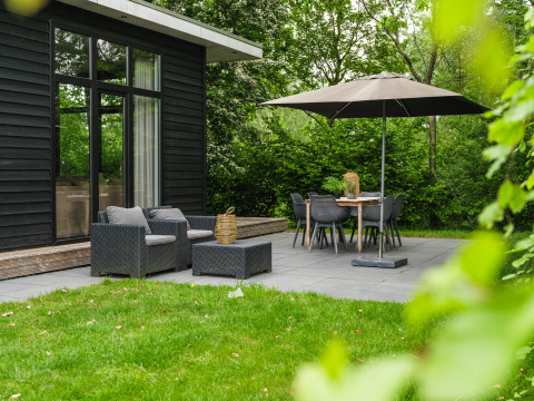 Outdoor terrace at River Cabin with lounge chairs, dining table and umbrella at Holiday Park Mölke in the Netherlands.