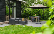Außenterrasse mit Sitzbereich und Esstisch unter Sonnenschirm an einer Flusshütte im Holiday Park Mölke, Niederlande.