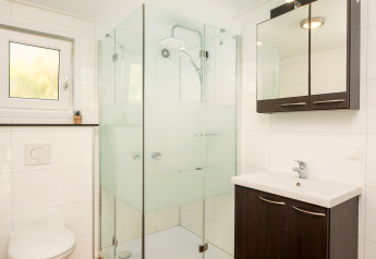 Baño moderno con suelo de madera, ducha de cristal, inodoro suspendido y lavabo en River Cabin met bubbeltub, Holiday Park Mölke.