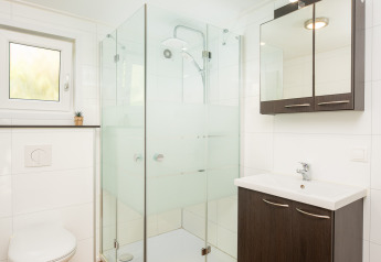 Bagno moderno con pavimento in legno, doccia in vetro, WC sospeso e lavabo in River Cabin met bubbeltub, Holiday Park Mölke.