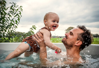 Un père s'amuse avec son bébé dans un jacuzzi extérieur à la River Cabin, Holiday Park Mölke, Pays-Bas.