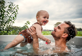 Un padre juega con su bebé en una bañera de hidromasaje al aire libre en River Cabin, Holiday Park Mölke, Países Bajos.