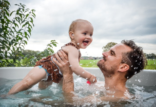 Un padre juega con su bebé en una bañera de hidromasaje al aire libre en River Cabin, Holiday Park Mölke, Países Bajos.