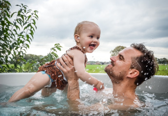 Un padre juega con su bebé en una bañera de hidromasaje al aire libre en River Cabin, Holiday Park Mölke, Países Bajos.