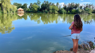 Une fille pêche au bord d’un lac paisible avec des arbres et un chalet en bois à Domaine des Feuilles.