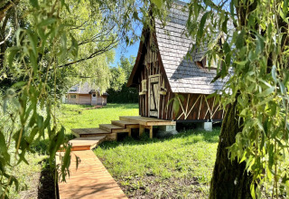 Holzhütte mit schrägem Dach und Holzsteg auf einer Wiese im Domaine des Feuilles, Auvergne-Rhône-Alpes, Frankreich.