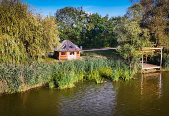 Cabine Boréalis situata sul lago, circondata da alberi e canne, sotto un cielo sereno e soleggiato.