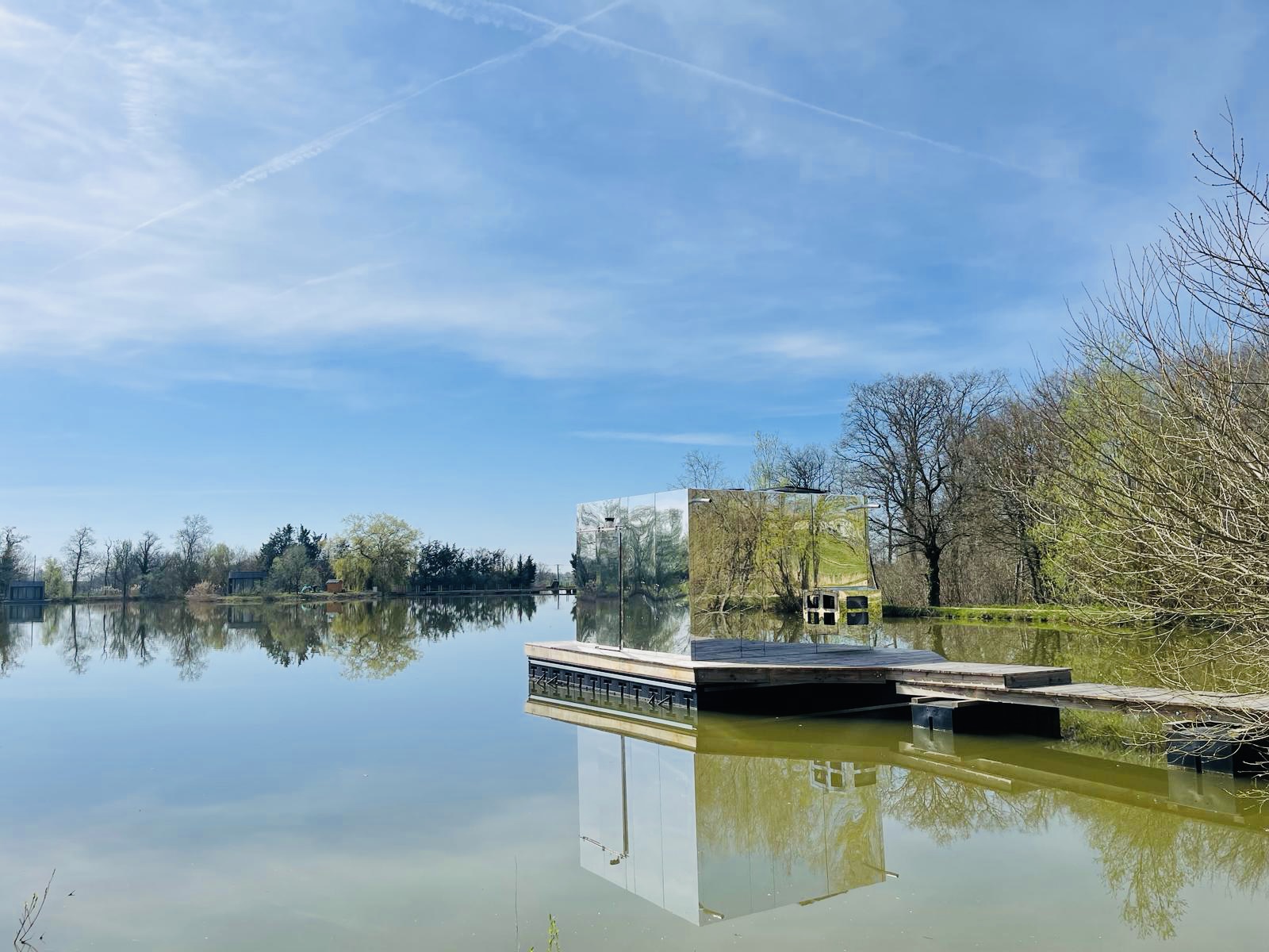 De spiegelcabine Cabine Spa Miroir weerspiegelt het rustige meerlandschap onder een heldere hemel.