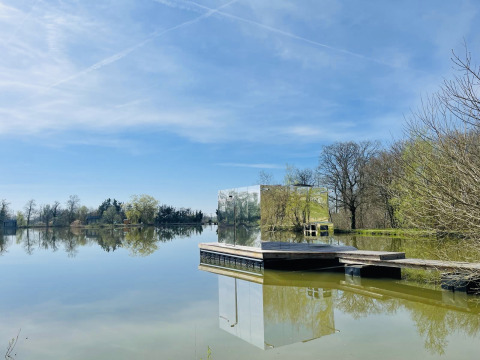 De spiegelcabine Cabine Spa Miroir reflecteert het vredige meerlandschap onder een blauwe lucht.