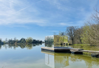 De spiegelcabine Cabine Spa Miroir reflecteert het vredige meerlandschap onder een blauwe lucht.