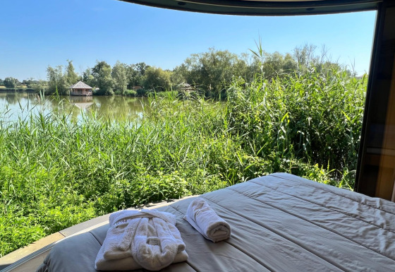 Uitzicht vanuit Lumipod île-hut met bed, groene natuur, een meer en een huisje in de verte.