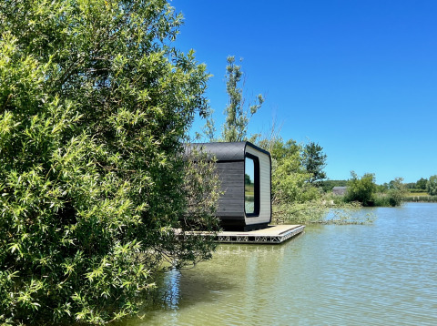 Moderne Héron-hut op een rustige vijver, deels verscholen achter bomen, bij zonnig mooi weer.