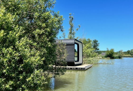 Moderne Héron-hut op een rustige vijver, deels verscholen achter bomen, bij zonnig mooi weer.