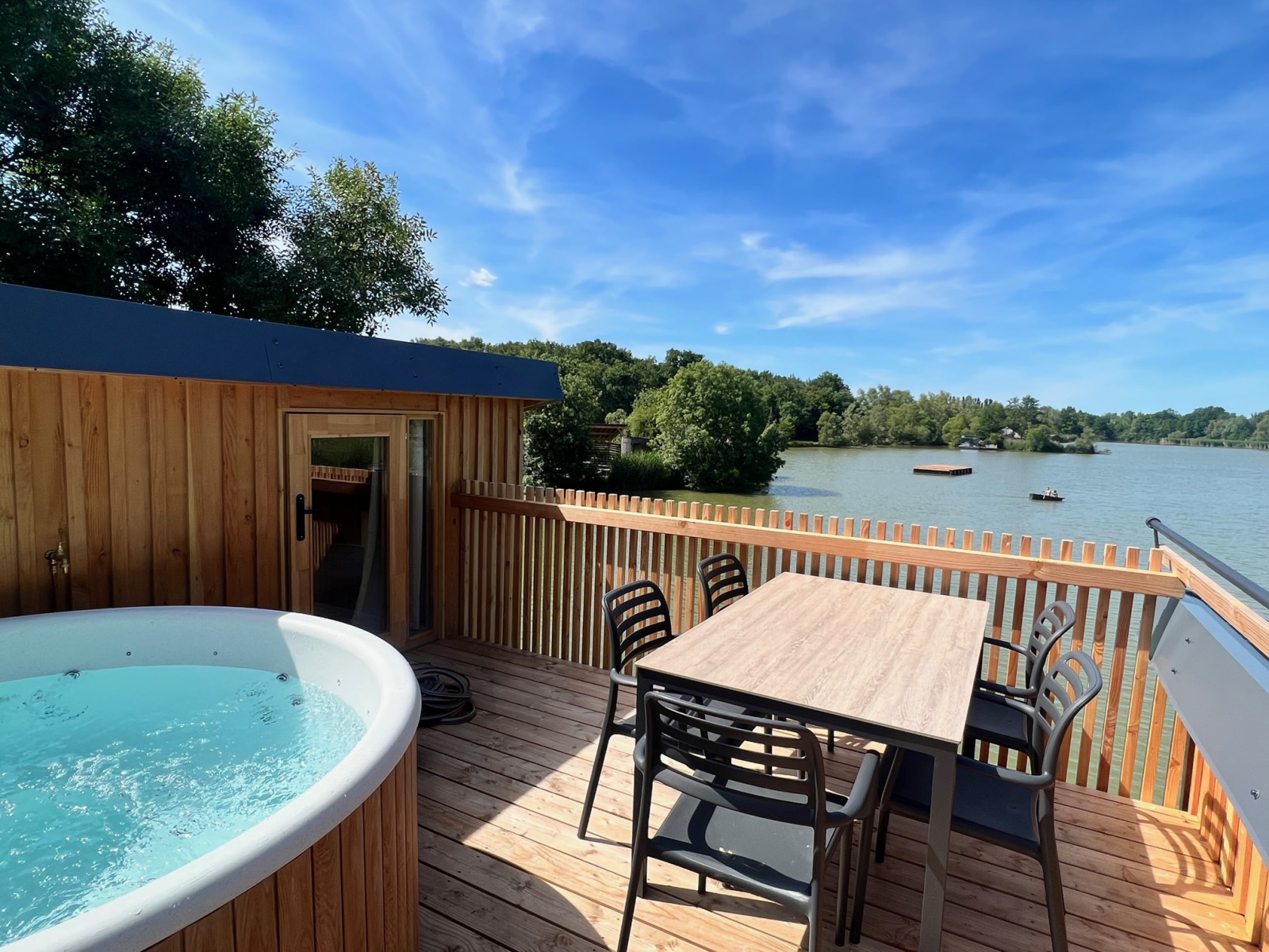 Buitenterras met bubbelbad en eettafel aan het meer bij Spa Horizon Cabin, Domaine des Feuilles, Frankrijk.