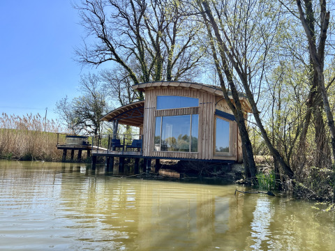 Moderne houten Spa Végétale Cabin aan het water met grote ramen en buitenterras met stoelen.