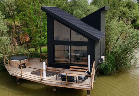 Spa Design Cabin, een moderne cabine met schuin dak op houten terras boven het water, omringd door groen.