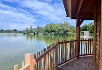 Blick von der Holzveranda der Cabine Ruche am Domaine des Feuilles mit See und Bäumen in Frankreich.