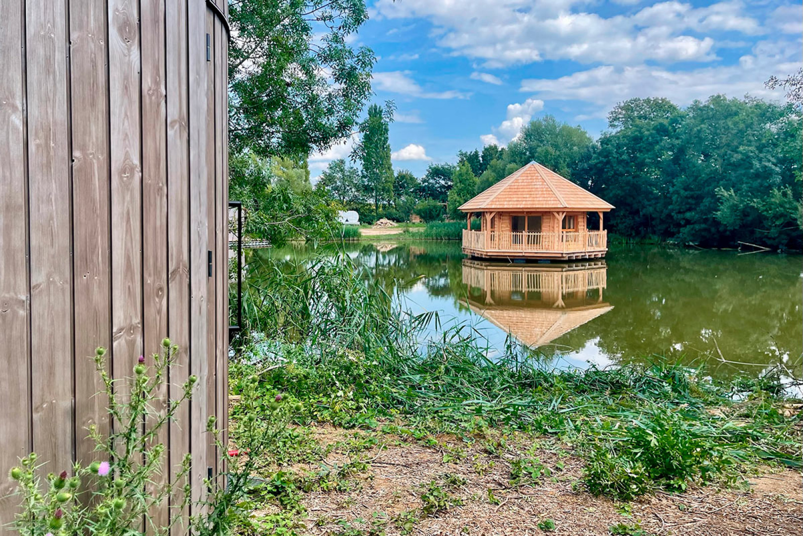 Uitzicht op een houten lodge en paviljoen op het meer bij Cabine Ruche, Domaine des Feuilles, Frankrijk op een zonnige dag.