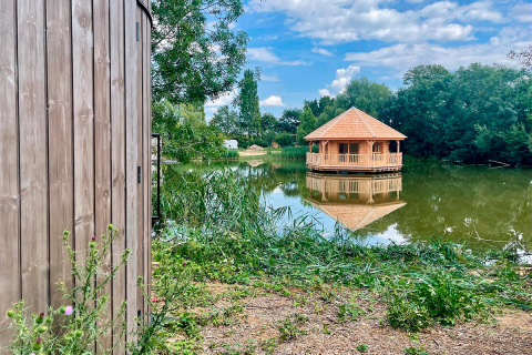 Zicht op een houten lodge en paviljoen op het meer bij Cabine Ruche, Domaine des Feuilles, Frankrijk op een zonnige dag.