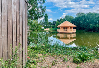 Blick auf eine Holzhütte und einen Pavillon am See bei Cabine Ruche, Domaine des Feuilles in Frankreich.