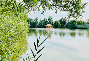 Blick auf See mit grüner Vegetation und Holzhütte bei Domaine des Feuilles, Cabine Ruche, Frankreich.