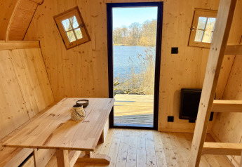 Interior de madera en la cabaña Cabine Fées, Domaine des Feuilles, Francia, con vista al lago exterior.