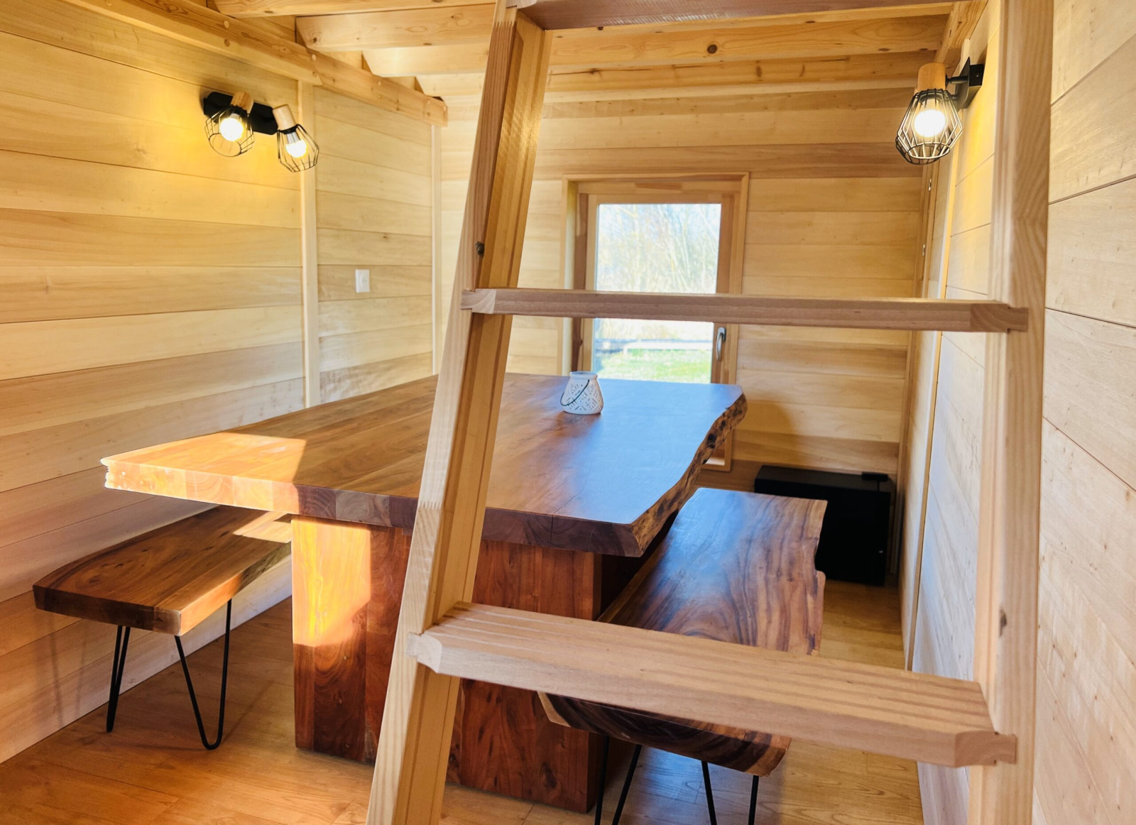 Interieur van Cabine Boréalis met houten tafel, banken en ladder in Domaine des Feuilles, Frankrijk.
