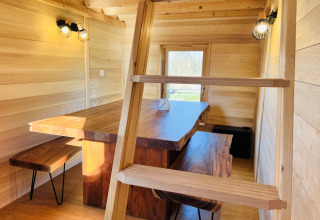 Interieur van Cabine Boréalis met houten tafel, banken en ladder bij Domaine des Feuilles in Frankrijk.
