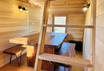 Interno di Cabine Boréalis con tavolo in legno, panche e scala al Domaine des Feuilles in Francia.