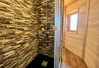 Doccia con pareti rivestite in pietra e porta in vetro alla Cabine Boréalis presso Domaine des Feuilles, Francia.