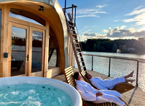 Twee personen in badjas genieten van ligstoelen naast een jacuzzi aan het water in Domaine des Feuilles.