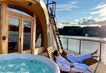Dos personas en albornoces descansan en tumbonas junto a una cabaña con jacuzzi en Domaine des Feuilles, Francia.