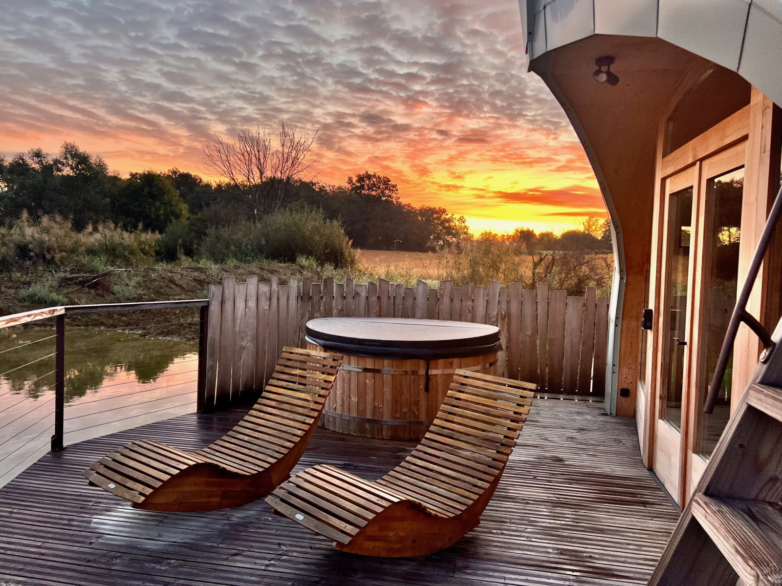 Zonsondergang bij Cabine Spa Les Flots, Domaine des Feuilles in Frankrijk, met houten stoelen en hottub op terras.