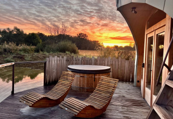 Vista del atardecer desde Cabine Spa Les Flots en Domaine des Feuilles, Francia, con sillas y jacuzzi en la terraza.