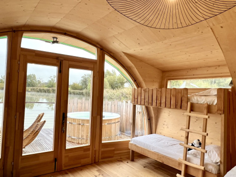 Binnenaanzicht van een houten hut met stapelbedden, grote ramen, terras en hot tub bij Domaine des Feuilles.