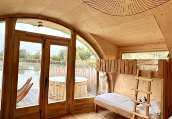 Interior de una cabaña de madera con literas, grandes puertas de cristal, terraza y jacuzzi en Domaine des Feuilles, Francia.