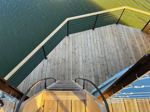 Uitzicht vanop een trap op een houten terras met leuning, boven water bij Cabine Spa Les Flots, Domaine des Feuilles, Frankrijk.