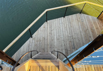 Vista desde una escalera a una terraza de madera con barandilla, sobre el agua en Cabine Spa Les Flots, Domaine des Feuilles, Francia.