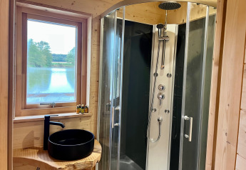Baño moderno en una cabaña de madera con ducha, lavabo negro y vista al lago en Cabine Spa Les Flots, Francia.